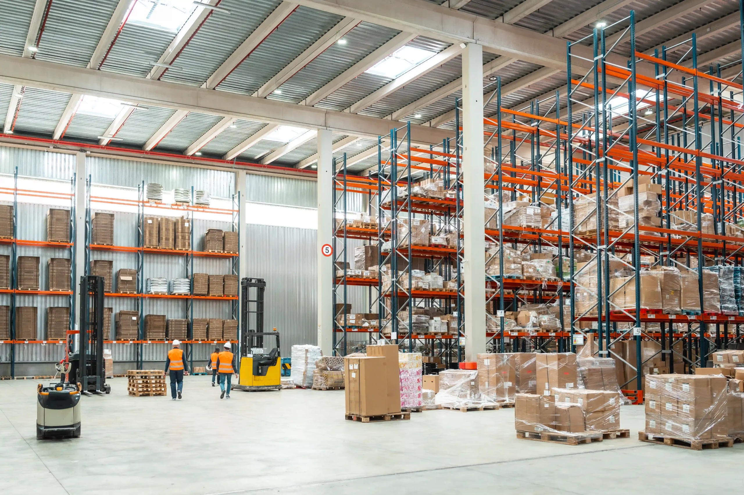 Racks of inventory and forklifts operating in a brightly lit cross docking distribution center